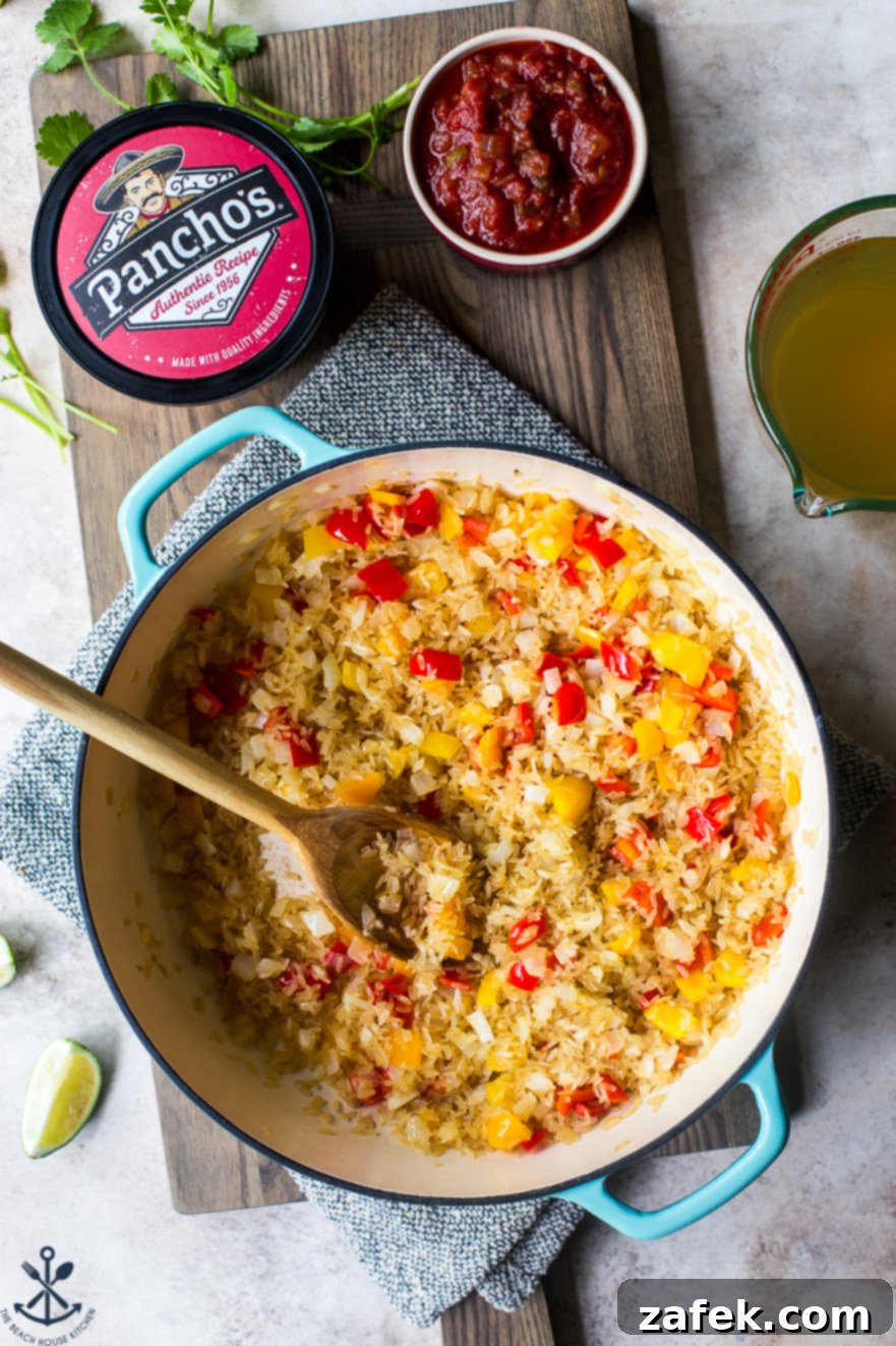 Up-close overhead photo of a skillet with pre-cooked rice, sautéed onions, and colorful bell peppers, illustrating a step in the cooking process