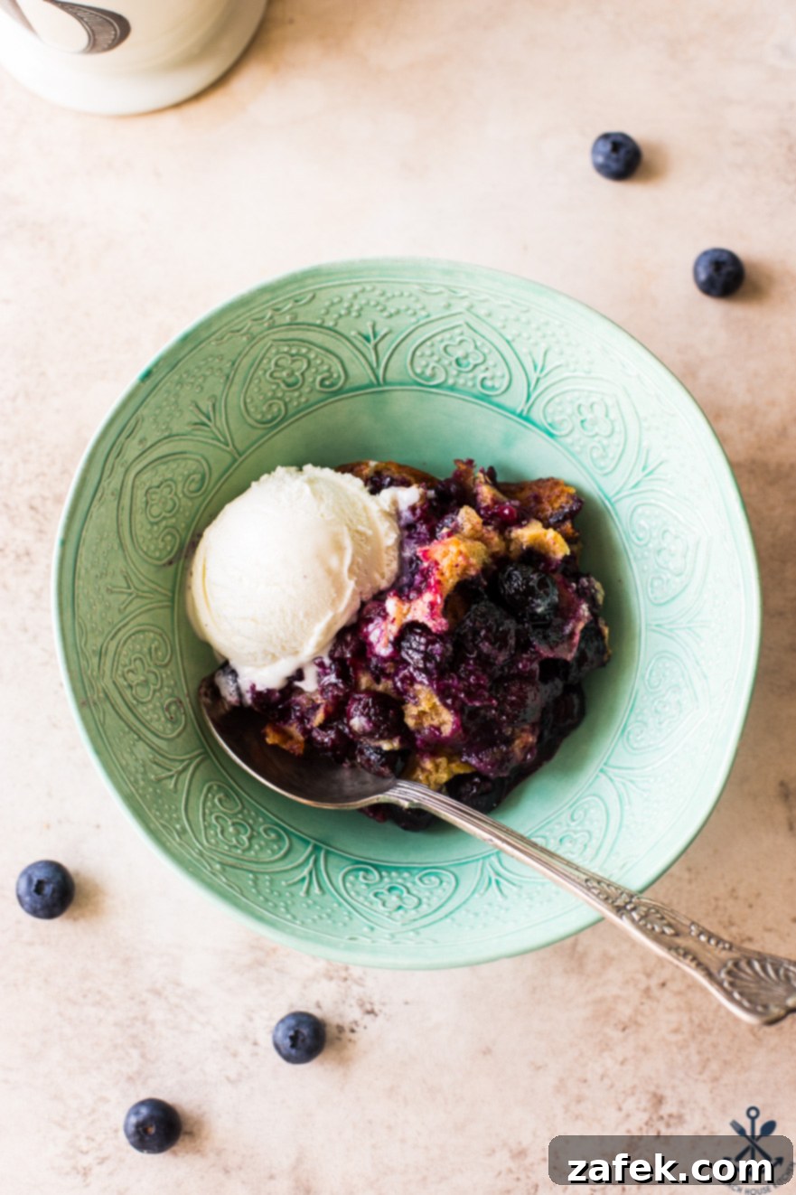 Overhead photo of a pale green bowl filled with perfectly baked Earl Grey blueberry cobbler, ready to be enjoyed