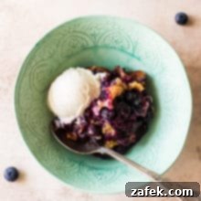 Overhead photo of a pale green bowl filled with Earl Grey Blueberry Cobbler, garnished with fresh blueberries