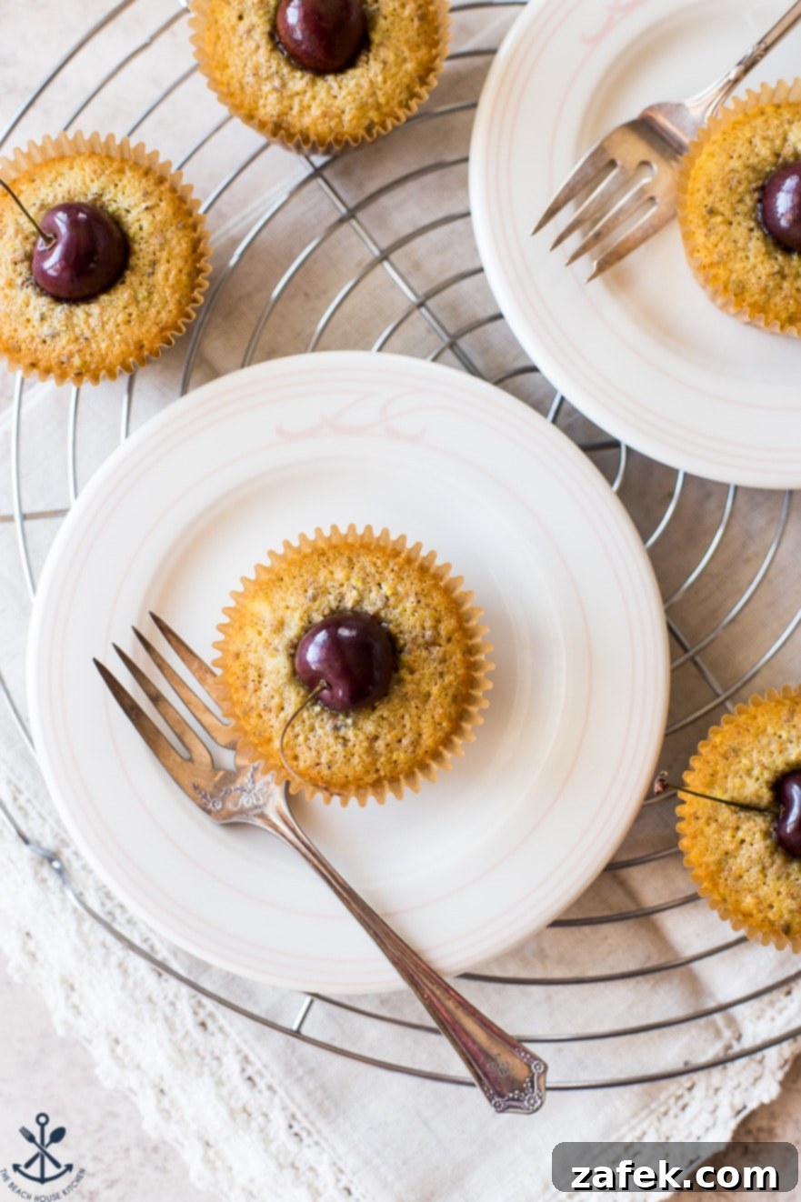 Dainty Cherry Pistachio Tea Cakes 3 A close-up overhead photo of a single Sweet Cherry Pistachio Tea Cake on a white plate with a fork, ready to be enjoyed.