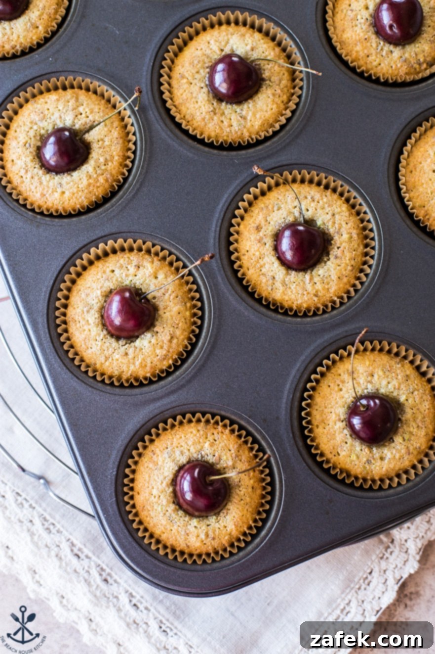 Dainty Cherry Pistachio Tea Cakes 4 A muffin tin filled with freshly baked Sweet Cherry Pistachio Tea Cakes, showing their perfectly puffed tops and vibrant cherry centers.
