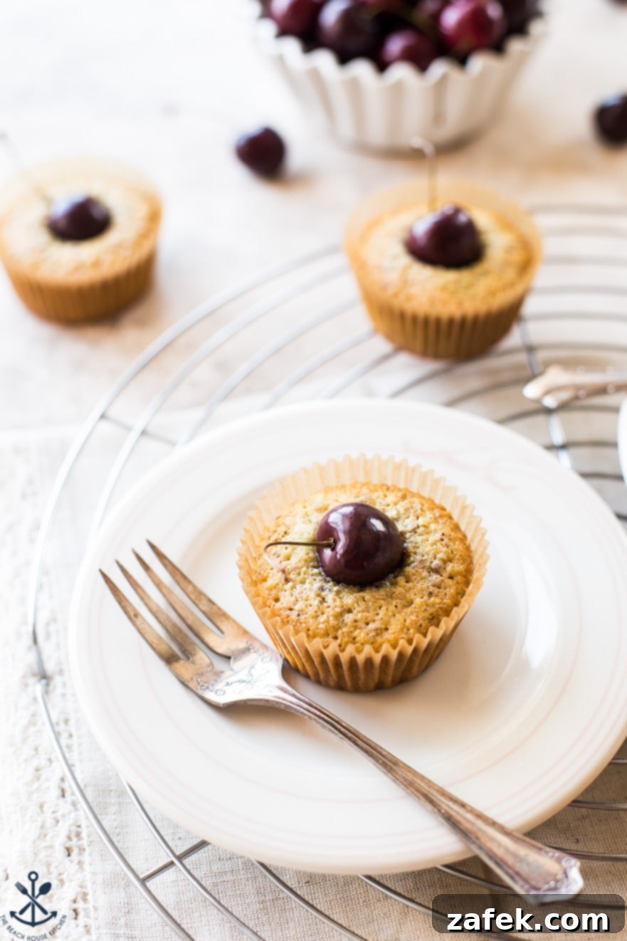 Dainty Cherry Pistachio Tea Cakes 5 A single Sweet Cherry Pistachio Tea Cake on a white plate with a silver fork, highlighting its delicate texture and the embedded cherry.