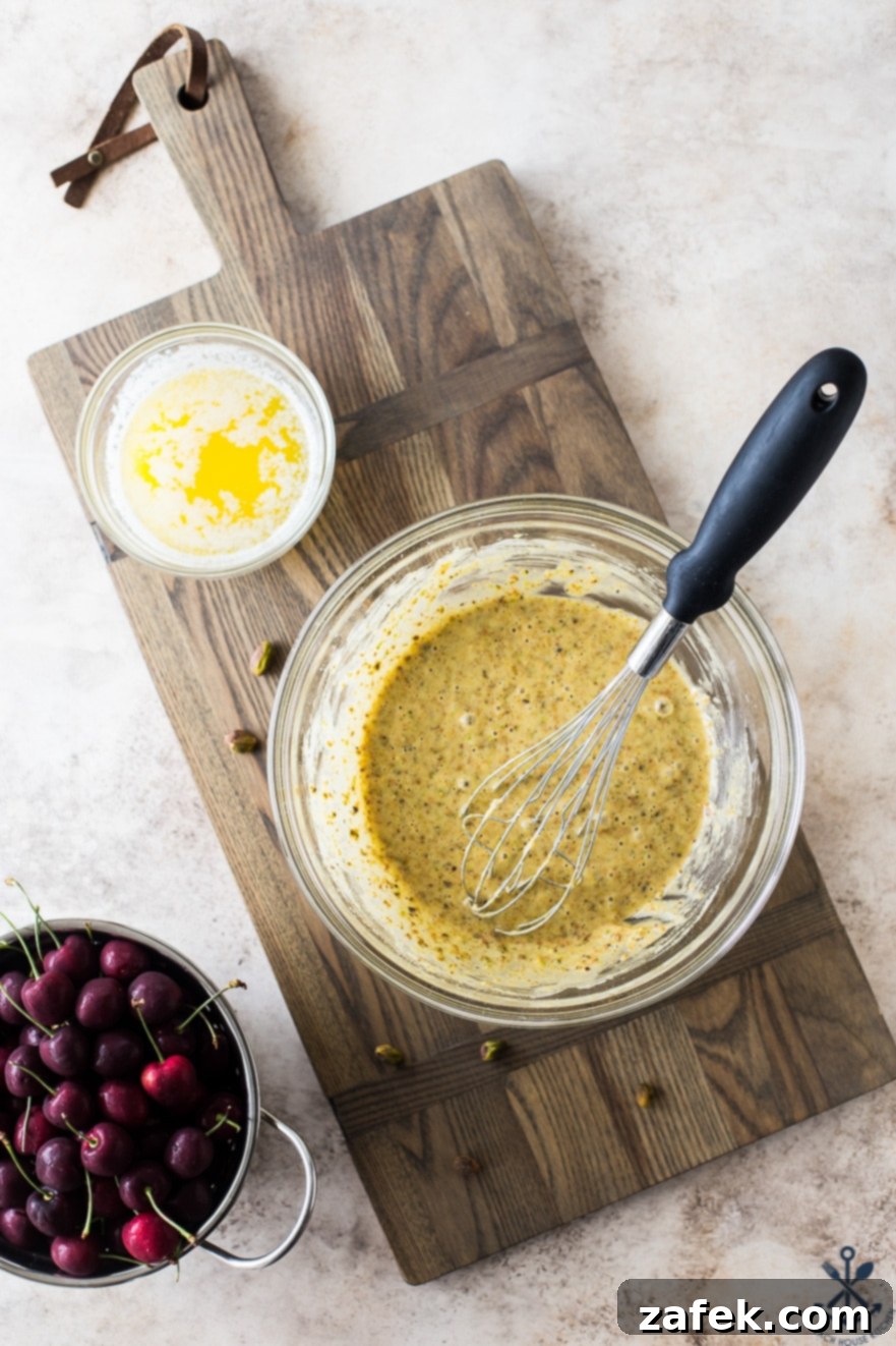 Dainty Cherry Pistachio Tea Cakes 8 A glass bowl containing the smooth, light green batter for Sweet Cherry Pistachio Tea Cakes, resting on a wooden surface, ready for baking.
