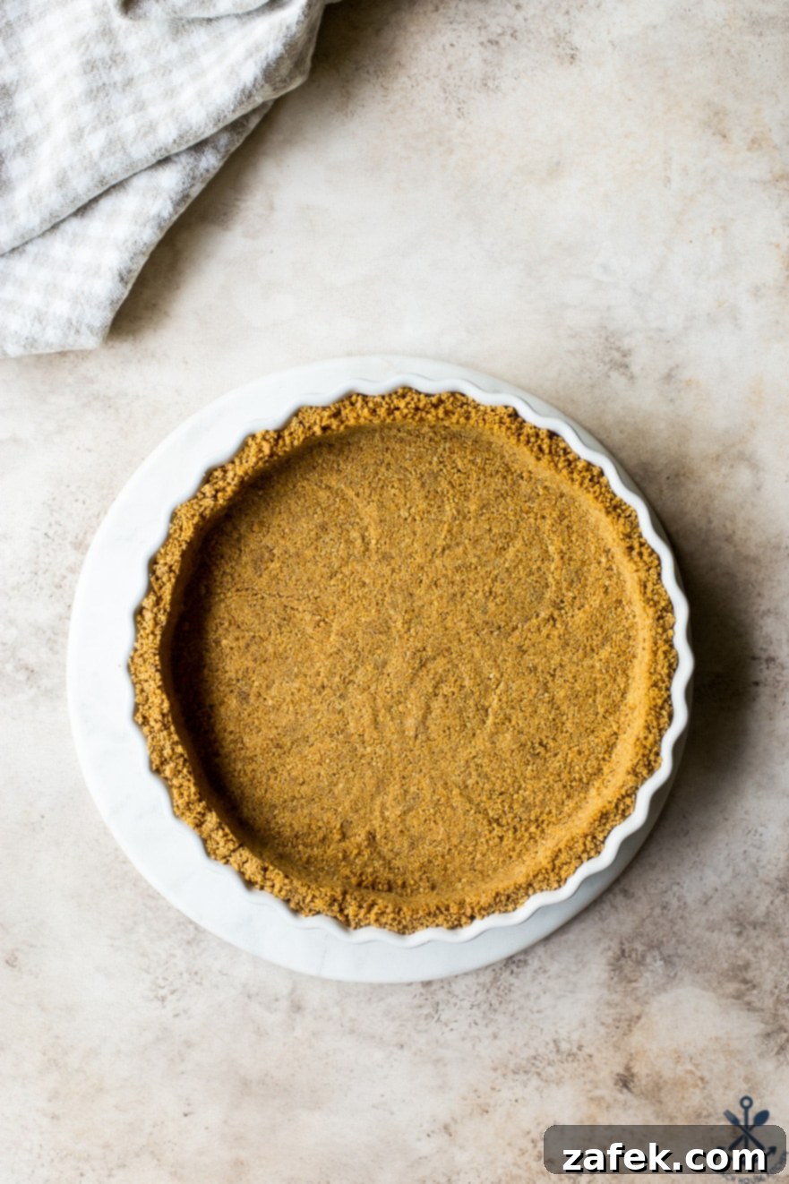 Zesty Orange Cream Tart 5 Overhead photo of a freshly baked graham cracker crust resting on a white round marble board, ready for the filling.