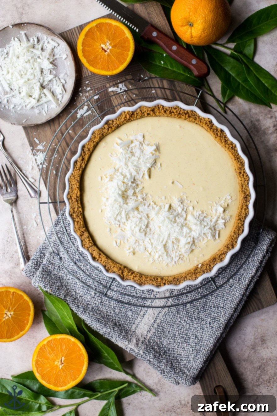 Zesty Orange Cream Tart 7 Overhead photo of an orange cream tart on a round wire rack, beautifully styled with fresh orange halves, creating a visually appealing summer scene.
