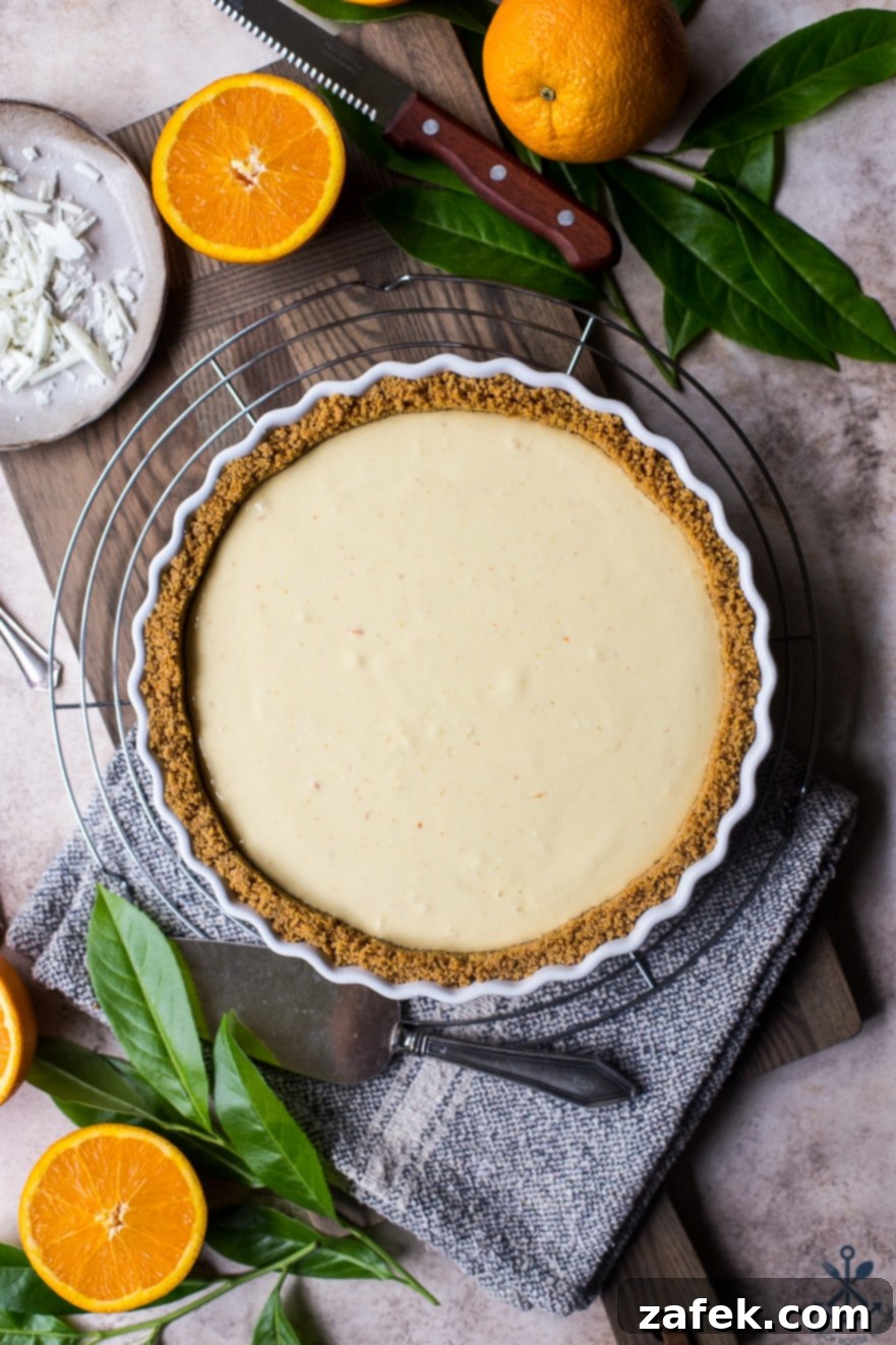 Zesty Orange Cream Tart 8 Overhead photo of an orange cream tart on a round wire rack, surrounded by fresh oranges, emphasizing its freshness and inviting presentation.