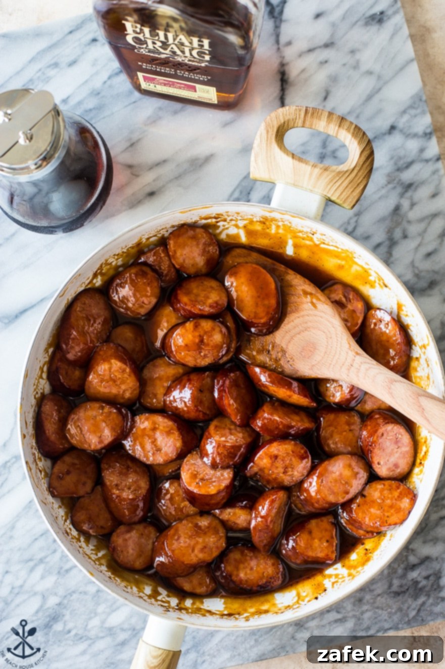 Maple Bourbon Glazed Kielbasa Bites 5 Overhead photo of a skillet filled with maple bourbon bbq kielbasa bites, glistening with sauce.