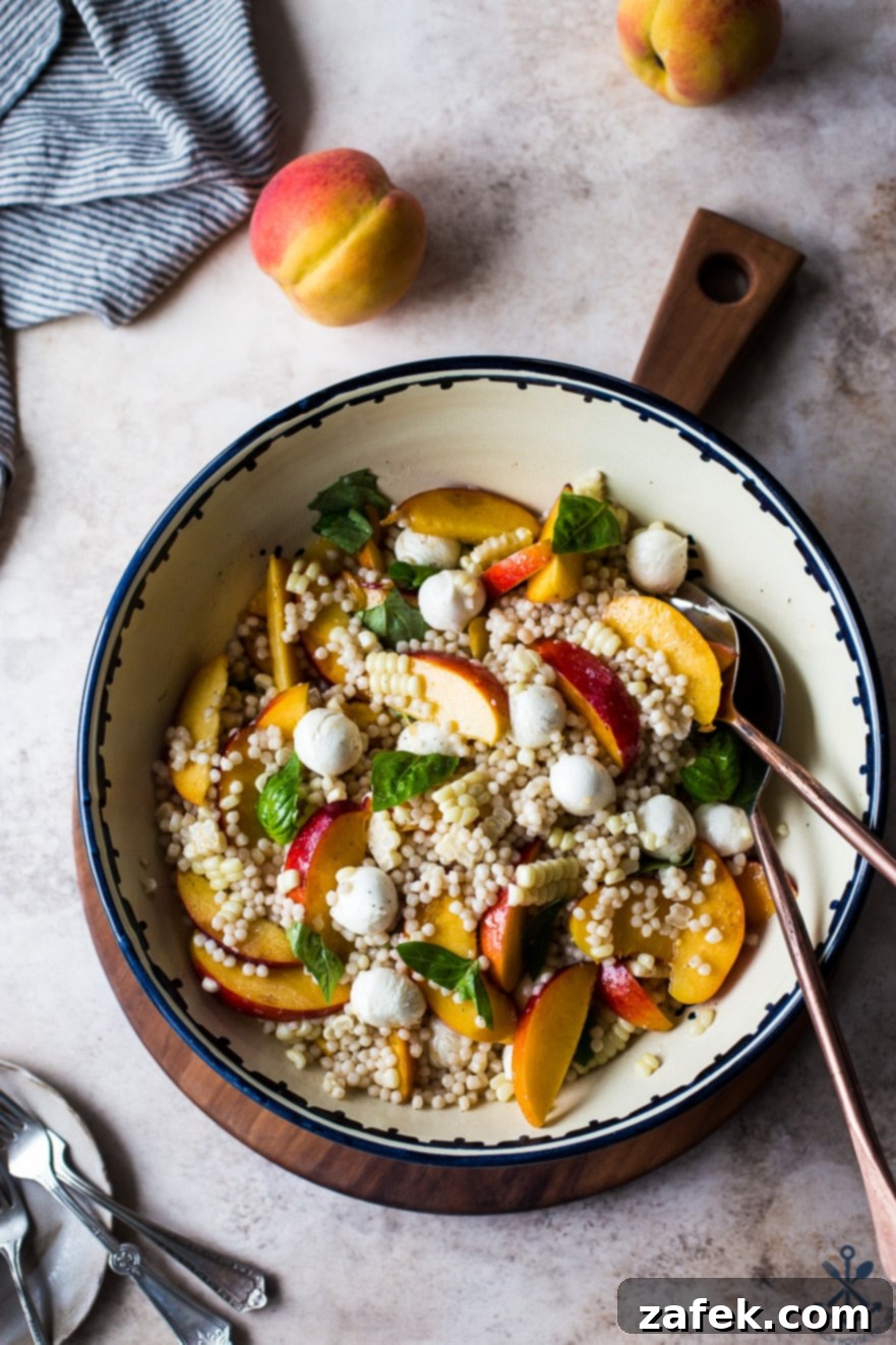 Peach Corn Caprese Couscous Salad in a bowl on a round wooden board, showcasing fresh ingredients