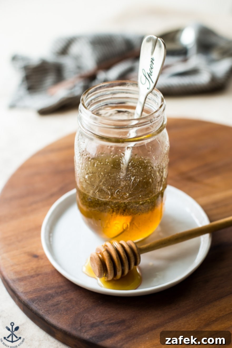 A clear glass jar filled with a golden white balsamic vinaigrette dressing on a white plate and wooden board