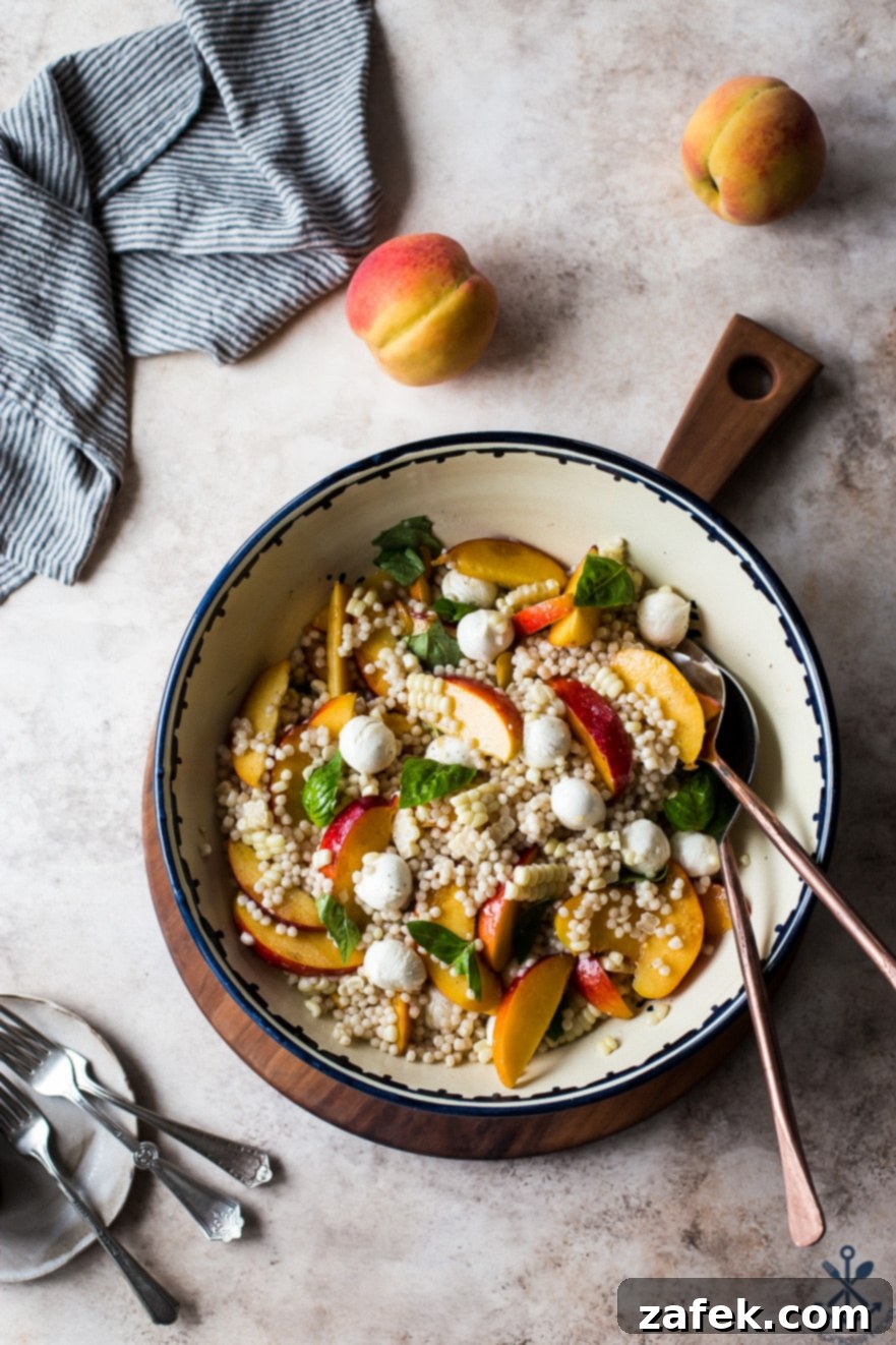 Overhead view of Peach Corn Caprese Couscous Salad served in a large white bowl on a wooden board