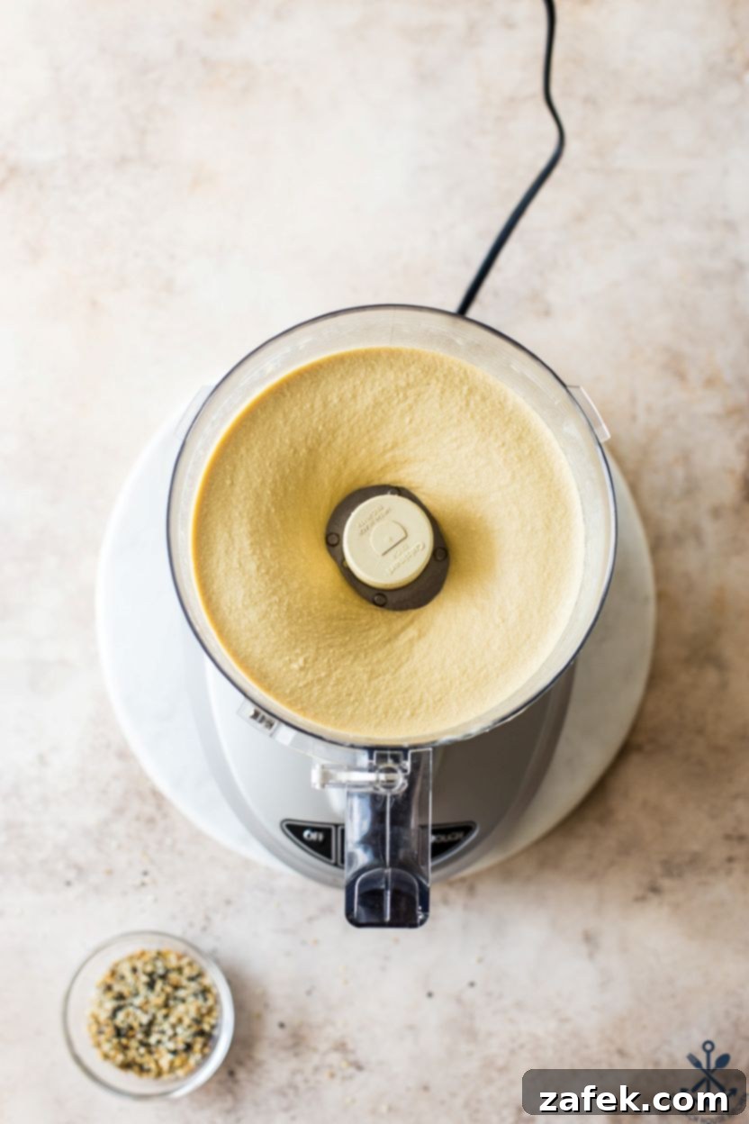 Hummus Unpacked 5 Overhead photo of a food processor containing tahini, olive oil, salt, garlic, and lemon juice, blended into a smooth paste.