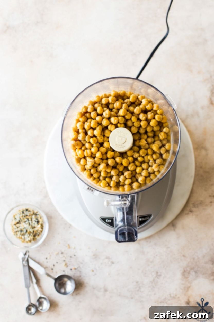 Hummus Unpacked 6 Overhead photo of a food processor filled with chickpeas and water, halfway through processing.