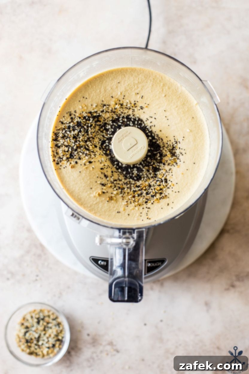 Hummus Unpacked 7 Overhead photo of a food processor filled with hummus, freshly topped with everything bagel seasoning.
