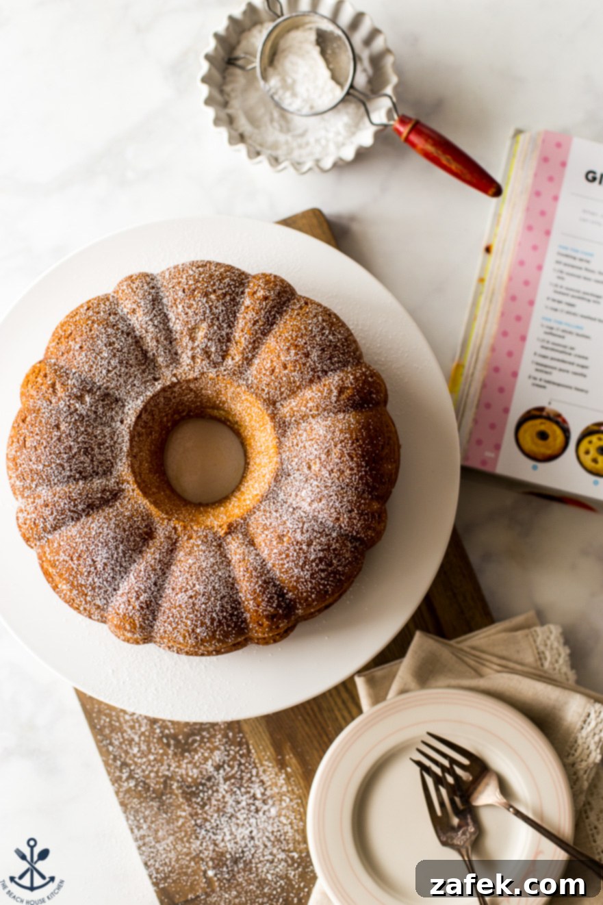Overhead photo of an Easy Twinkie Bundt Cake on a white cake plate on a wooden board, showcasing its golden exterior and inviting shape.