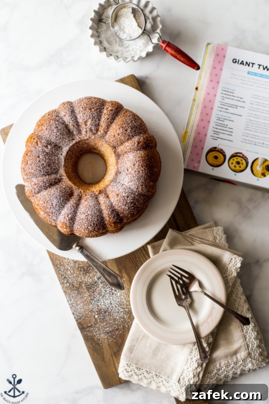 Overhead close-up of the Easy Twinkie Bundt Cake, glistening with a light dusting of powdered sugar, presented on an elegant white cake plate.