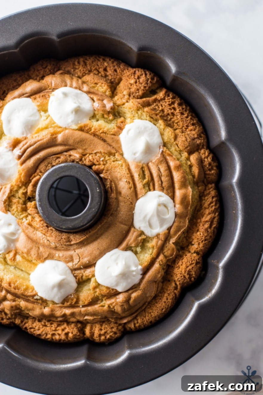 Two enticing slices of Easy Twinkie Bundt Cake, each showing off its golden cake and creamy filling, presented on small white plates on a rustic wooden surface.