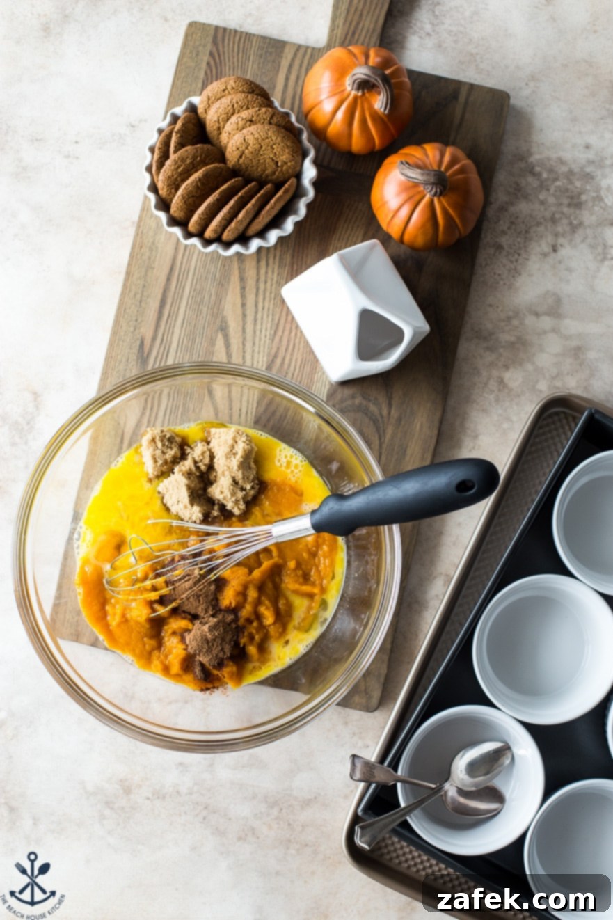 Spiced Pumpkin Custards with Gingersnap Crumble 4 A bowl filled with the vibrant orange custard batter, surrounded by key ingredients like eggs, heavy cream, and pumpkin puree, ready to be mixed.