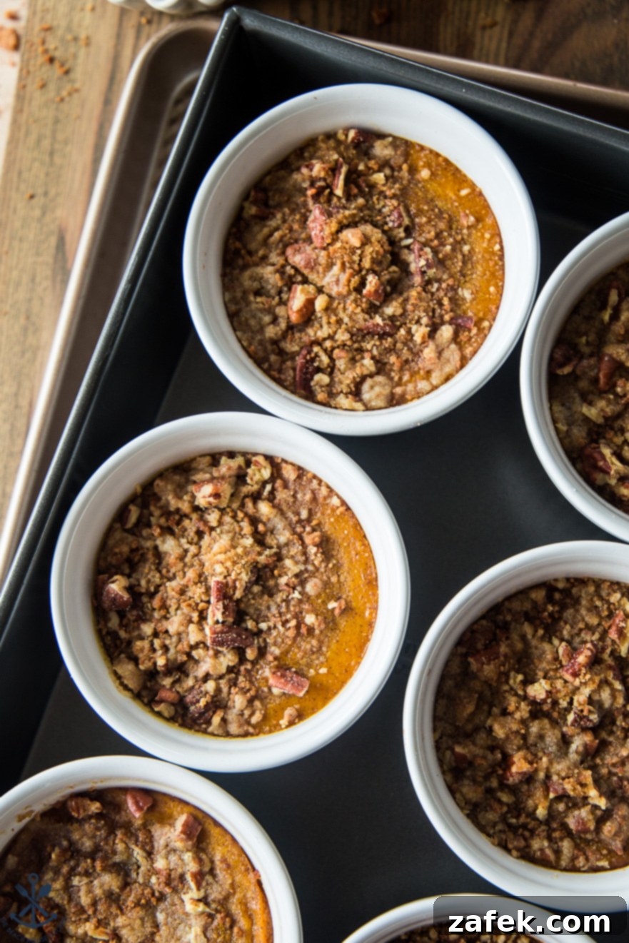 Spiced Pumpkin Custards with Gingersnap Crumble 6 White ramekins containing pumpkin custards submerged in a hot water bath within a large roasting pan, ready for baking.