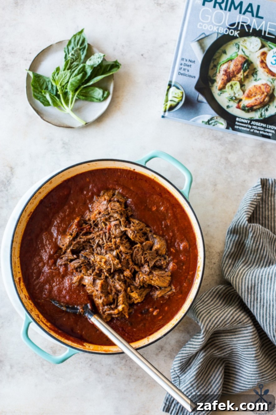 Unforgettable Short Rib Ragù Unmissable Giveaway 7 A closer look at the finished Short Rib Ragù in a Dutch oven, garnished with fresh basil leaves, alongside The Primal Gourmet Cookbook, ready to inspire.