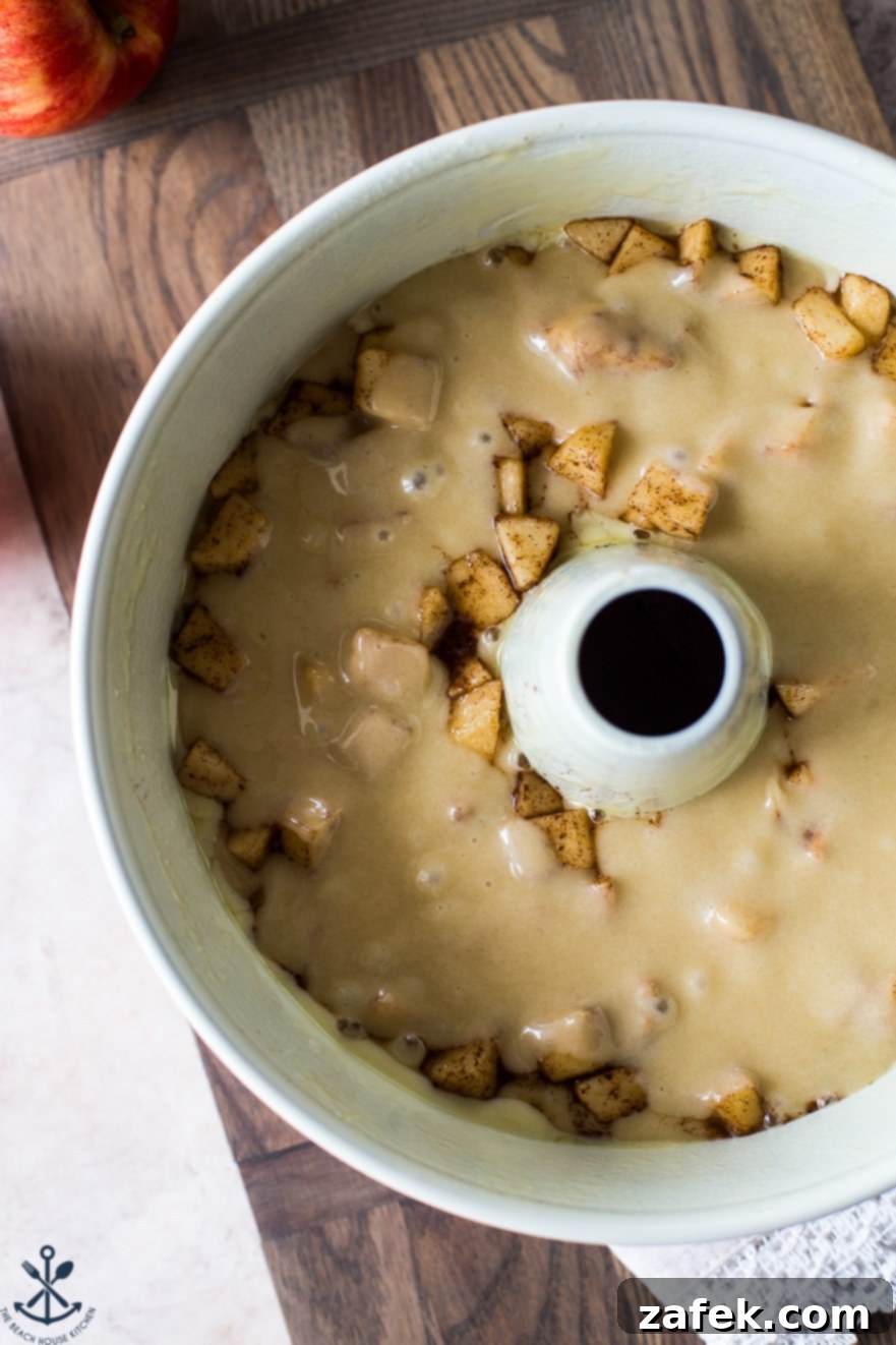 Old Fashioned Apple Spice Cake 7 An overhead view of the cake batter expertly layered with cinnamon-sugar coated apples in a tube pan, halfway through the preparation process, ready for the oven.
