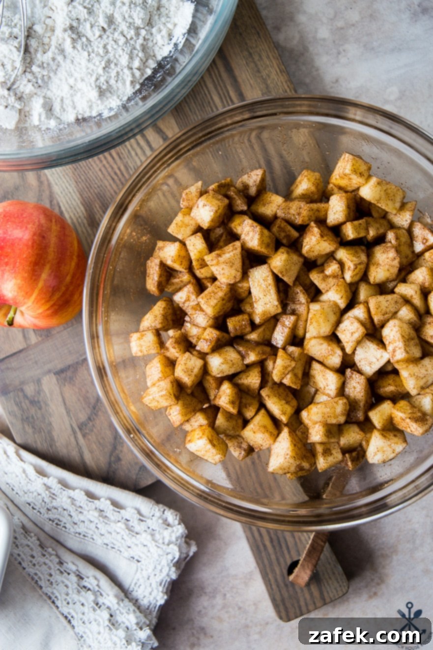 Old Fashioned Apple Spice Cake 10 An overhead shot of a clear glass bowl generously filled with peeled, diced apple chunks, perfectly coated in a sweet cinnamon sugar mixture, ready for baking.