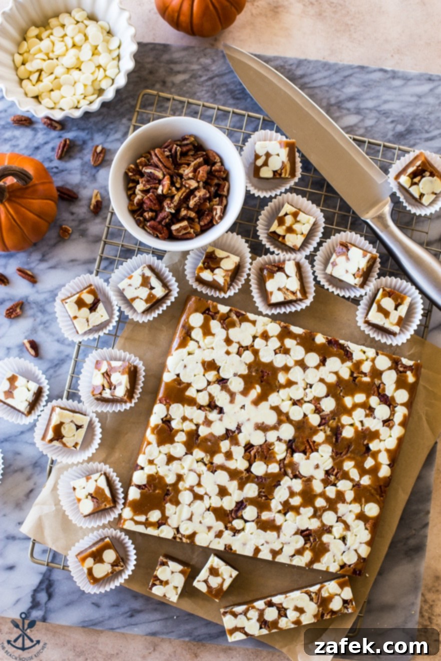 Overhead photo of a marble board featuring a slab of Pumpkin Spice White Chocolate Pecan Caramels ready for cutting, alongside individual caramels in white paper cups.