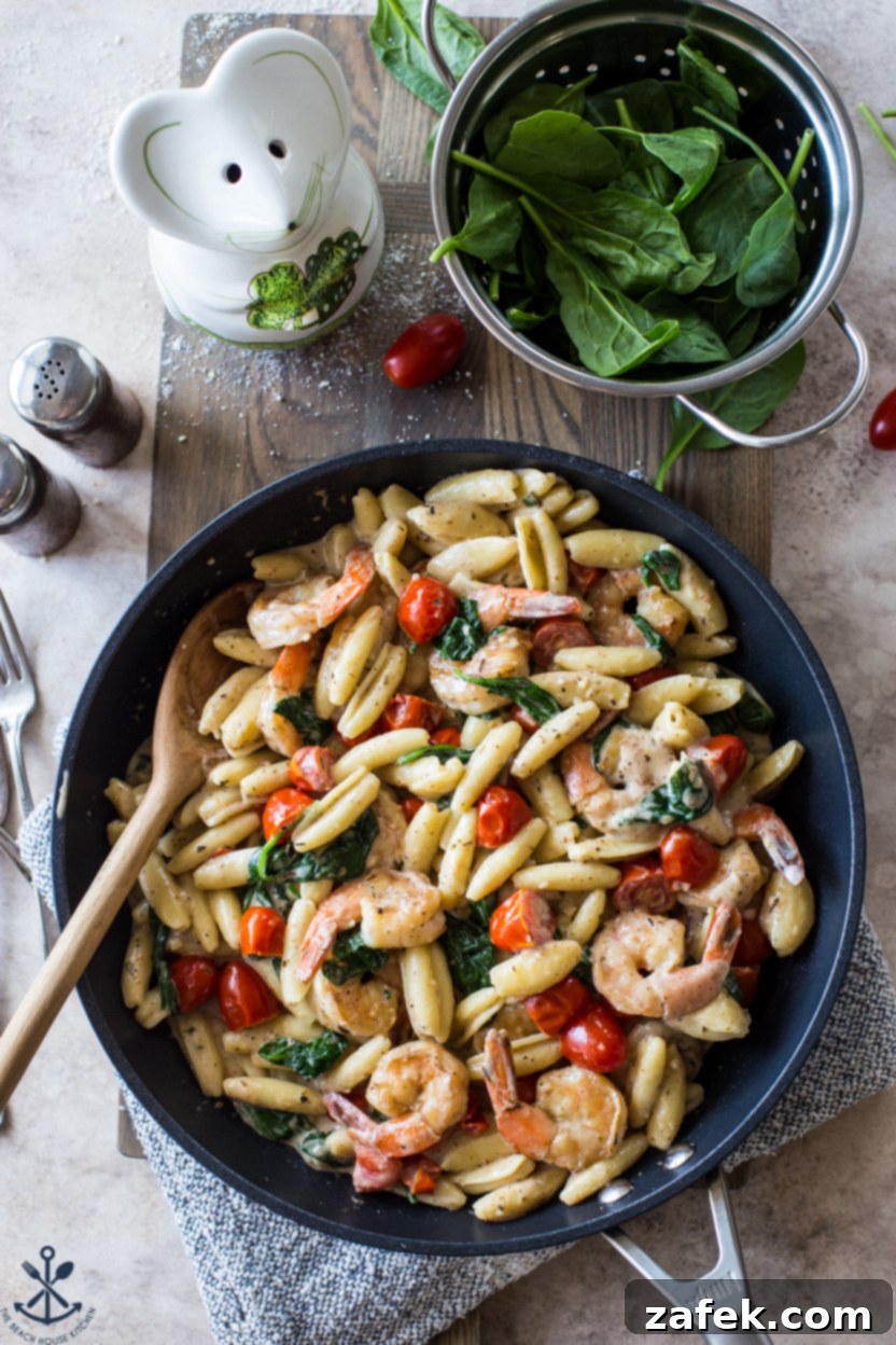 Creamy Garlic Shrimp Pasta with Sun-Kissed Tomatoes and Tender Spinach 5 Overhead photo of a skillet full of cooked Shrimp Pasta with Garlic Cream Sauce, Tomatoes, and Spinach, garnished with fresh herbs, ready to be served.