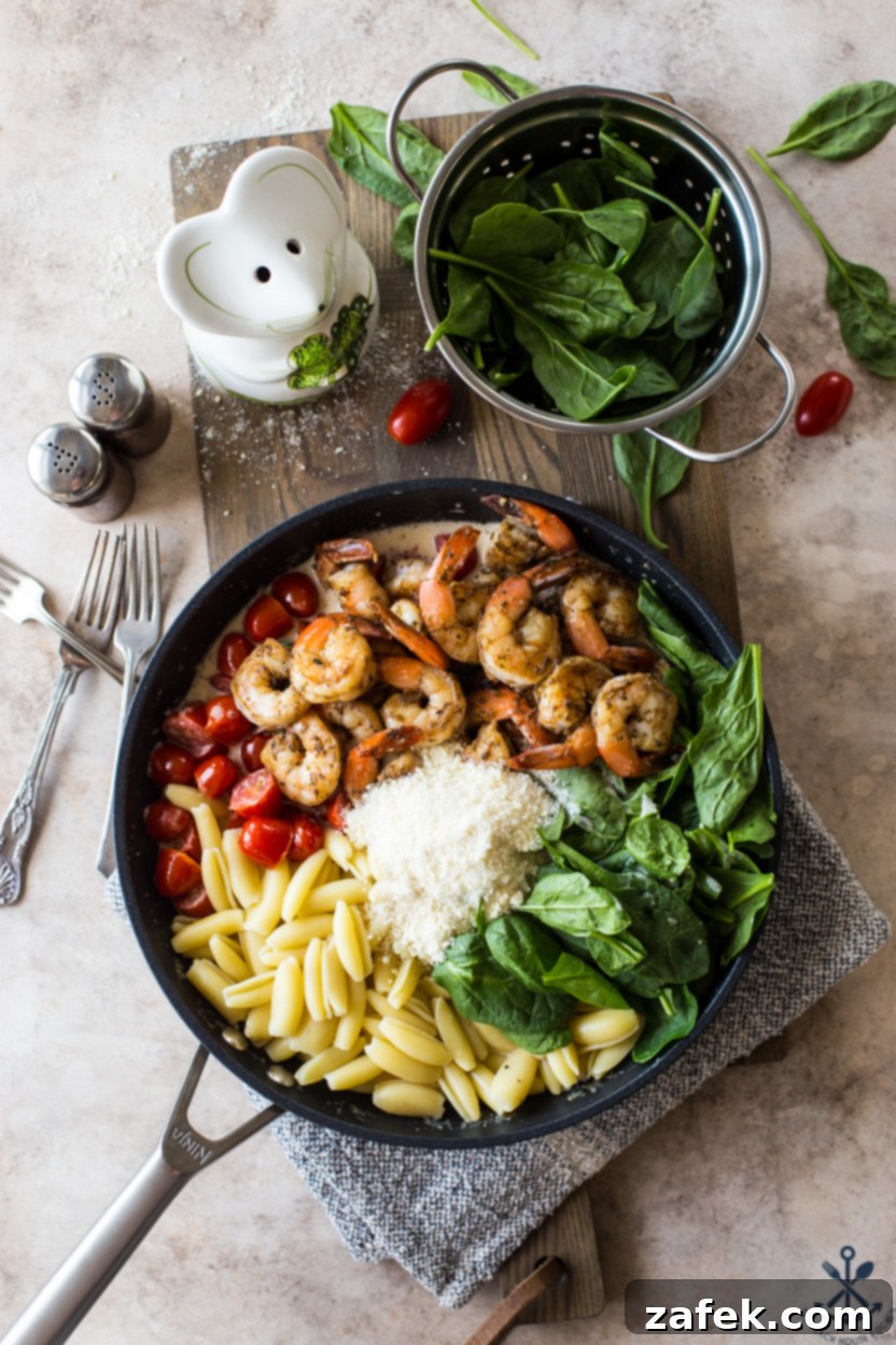 Creamy Garlic Shrimp Pasta with Sun-Kissed Tomatoes and Tender Spinach 6 Overhead photo of a skillet of pasta, shrimp, and vegetables before they are fully mixed, showing the separate components ready to be combined.