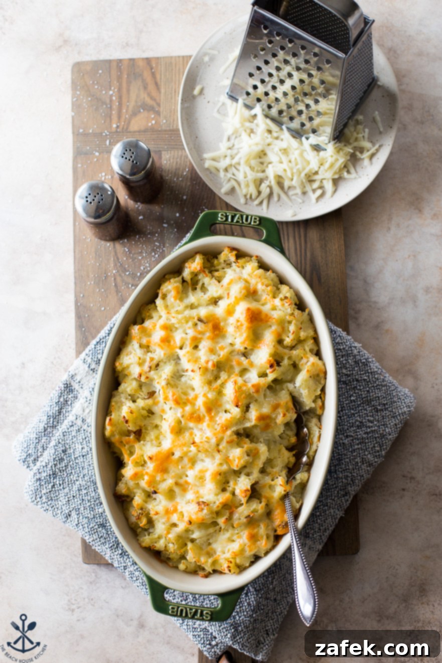 Potatoes Romanoff in an oval baking dish with a plate of shredded cheese and a grater