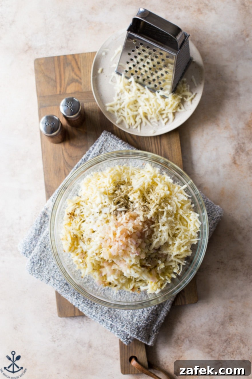 Overhead photo of ingredients for potato dish in a glass bowl with a plate of shredded cheese and a grater