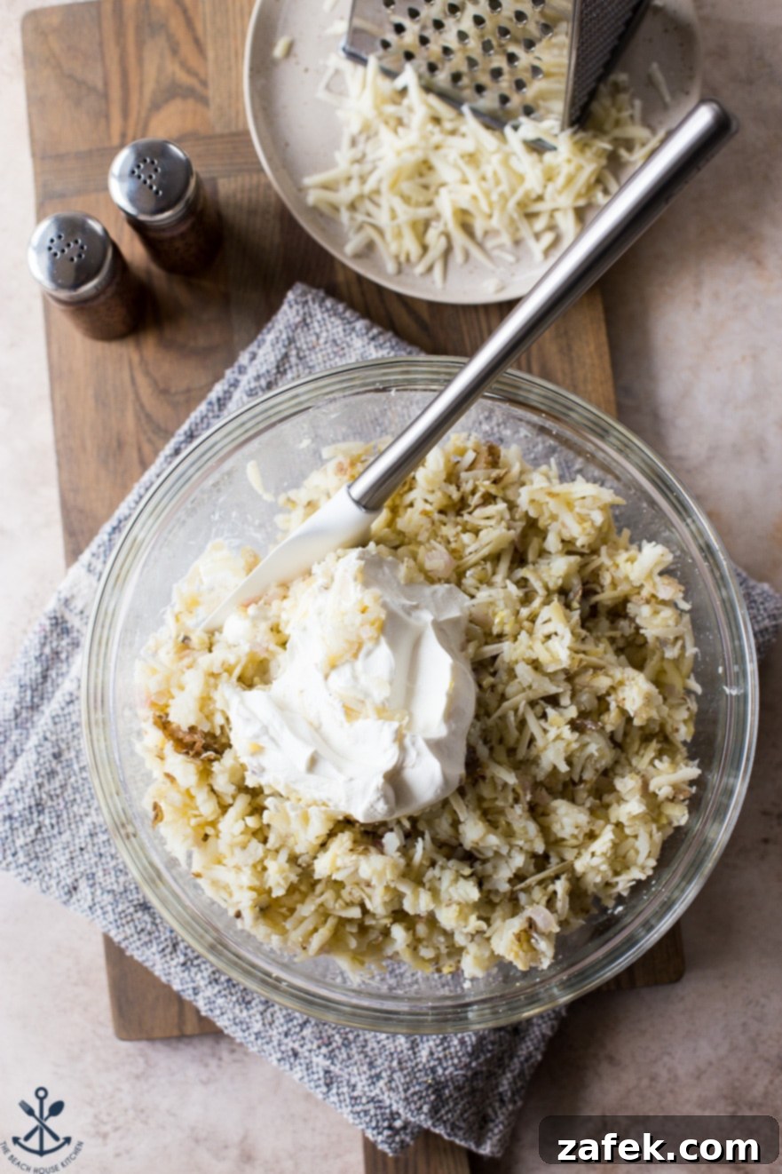 Overhead photo of glass bowl filled with shredded potatoes and sour cream with a spatula