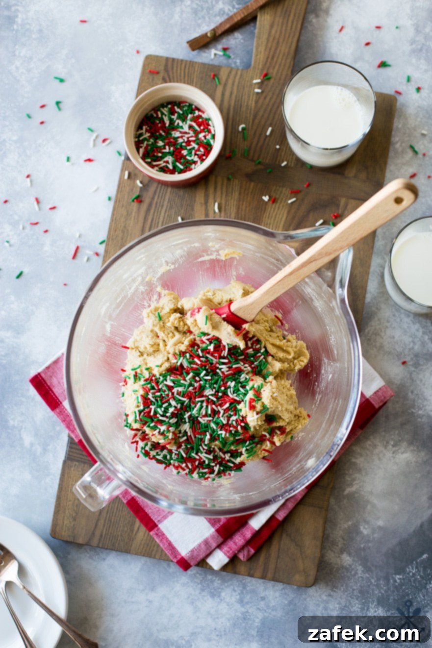One-Pan Holiday Funfetti Cookie Bliss 4 Overhead photo of sugar cookie dough in a glass bowl with a spatula, ready to be spread into a skillet, set on a wooden board