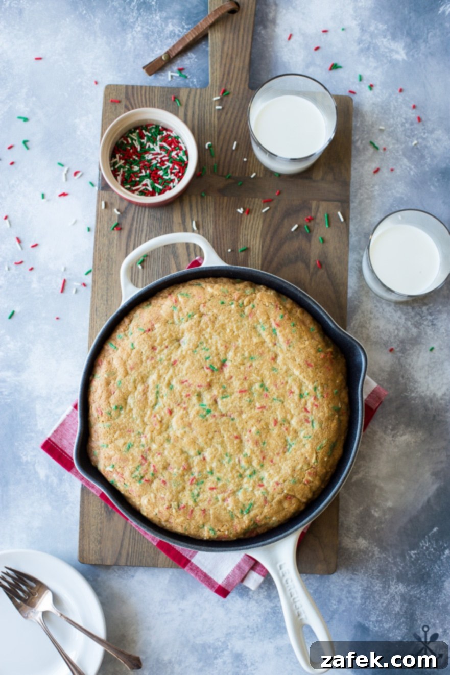 One-Pan Holiday Funfetti Cookie Bliss 7 Overhead photo of a fully decorated sugar cookie skillet with icing and extra sprinkles, ready for serving, on a wooden board