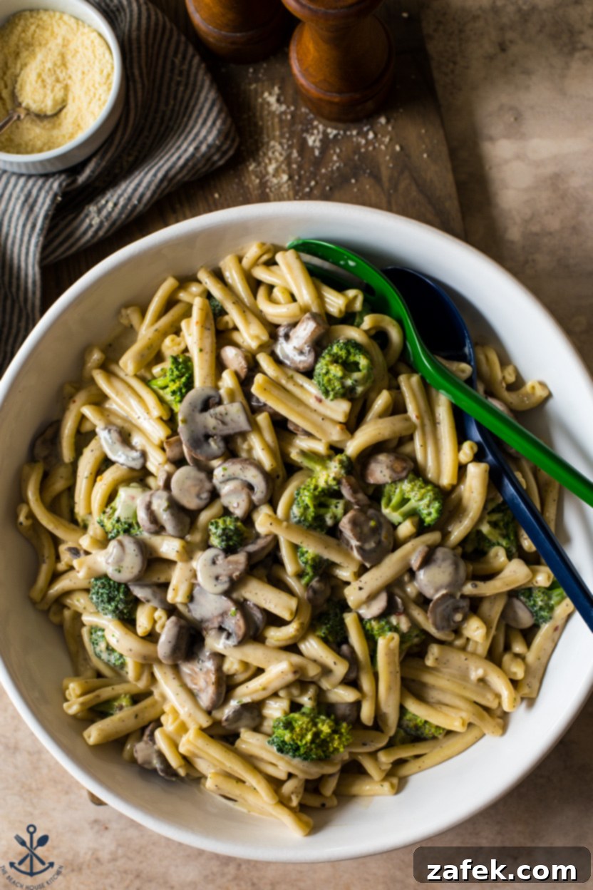 Creamy Garlic Pasta with Broccoli and Mushrooms 2 Overhead shot of a white platter filled with creamy garlic broccoli mushroom pasta, garnished with fresh herbs and a sprinkle of Parmesan.