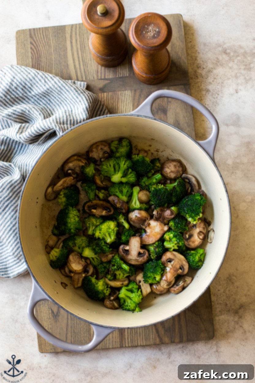 Creamy Garlic Pasta with Broccoli and Mushrooms 5 Close-up overhead photo of a pot containing sautéed broccoli florets and sliced mushrooms, glistening with butter.