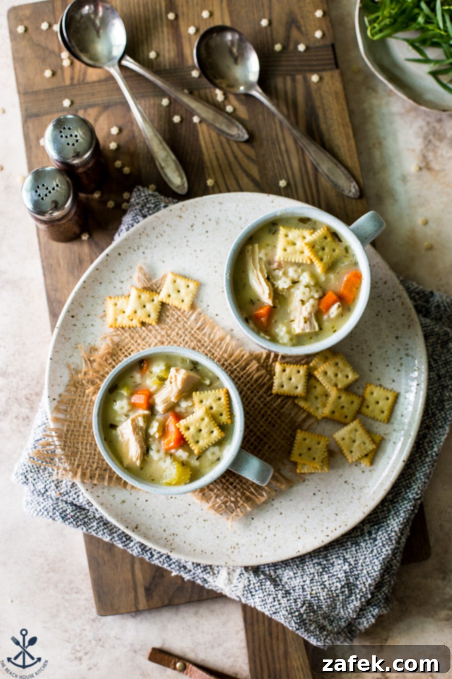 Overhead photo of two mugs filled with chicken soup with stars on a plate with saltine crackers