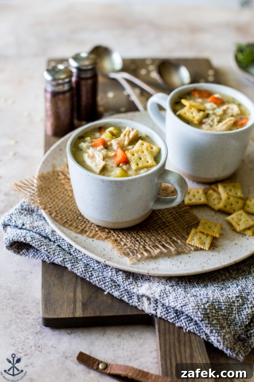 Two mugs filled with chicken soup on a plate with saltines