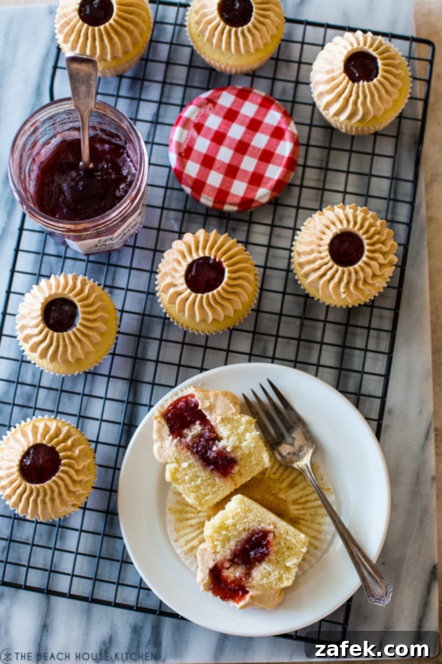 Overhead photo of cupcakes on a wire rack with one cupcake halved on a white plate, revealing the jelly filling