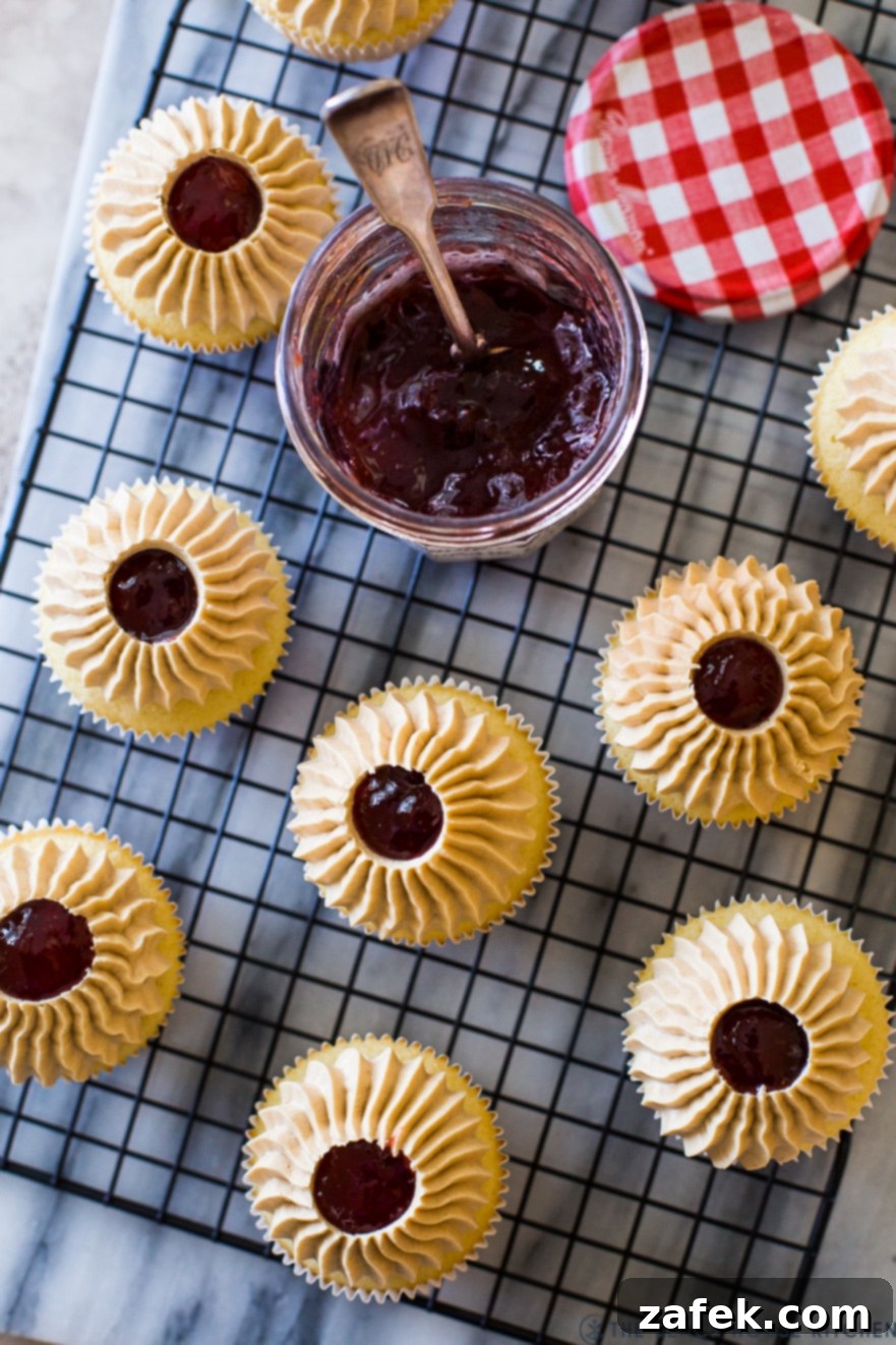 Up close overhead photo of a freshly baked cupcake on a wire rack next to a jar of strawberry preserves