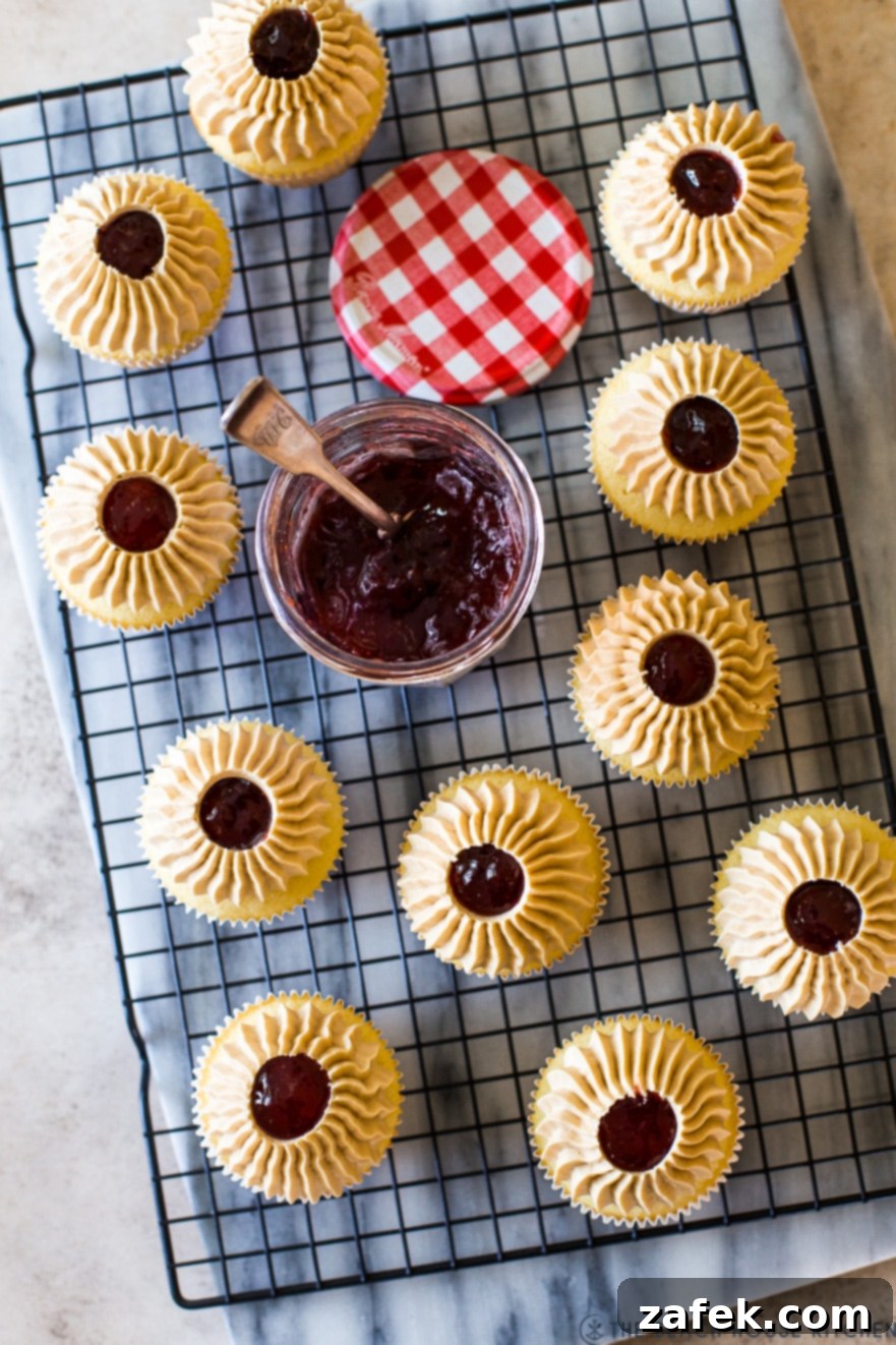Overhead photo of finished Peanut Butter and Jelly Cupcakes on a wire rack with a jar of preserves in the background, ready to be enjoyed
