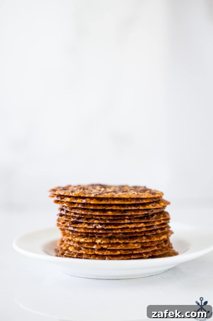 A stack of golden brown, thin pecan coconut lace cookies on a white plate