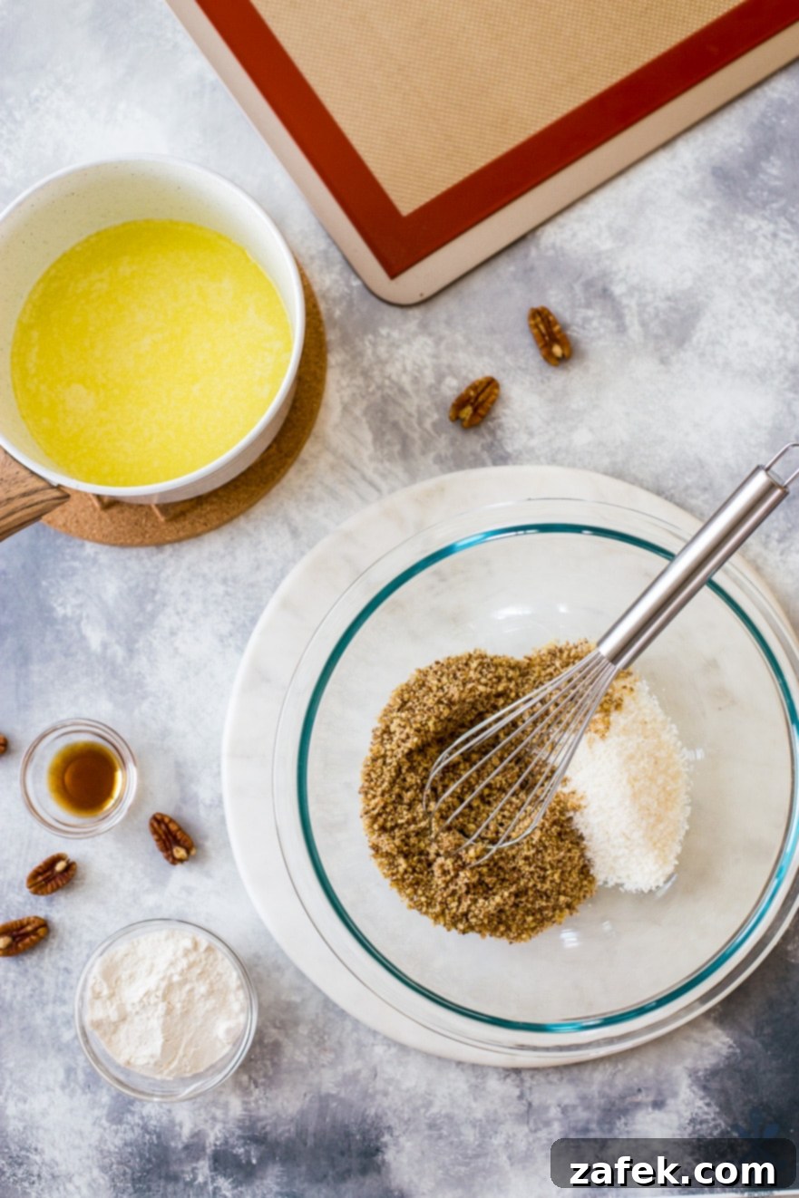 Overhead photo of ingredients for pecan coconut lace cookies, including butter, sugar, corn syrup, flour, pecans, coconut, and vanilla extract, arranged in small glass bowls on a grayish background