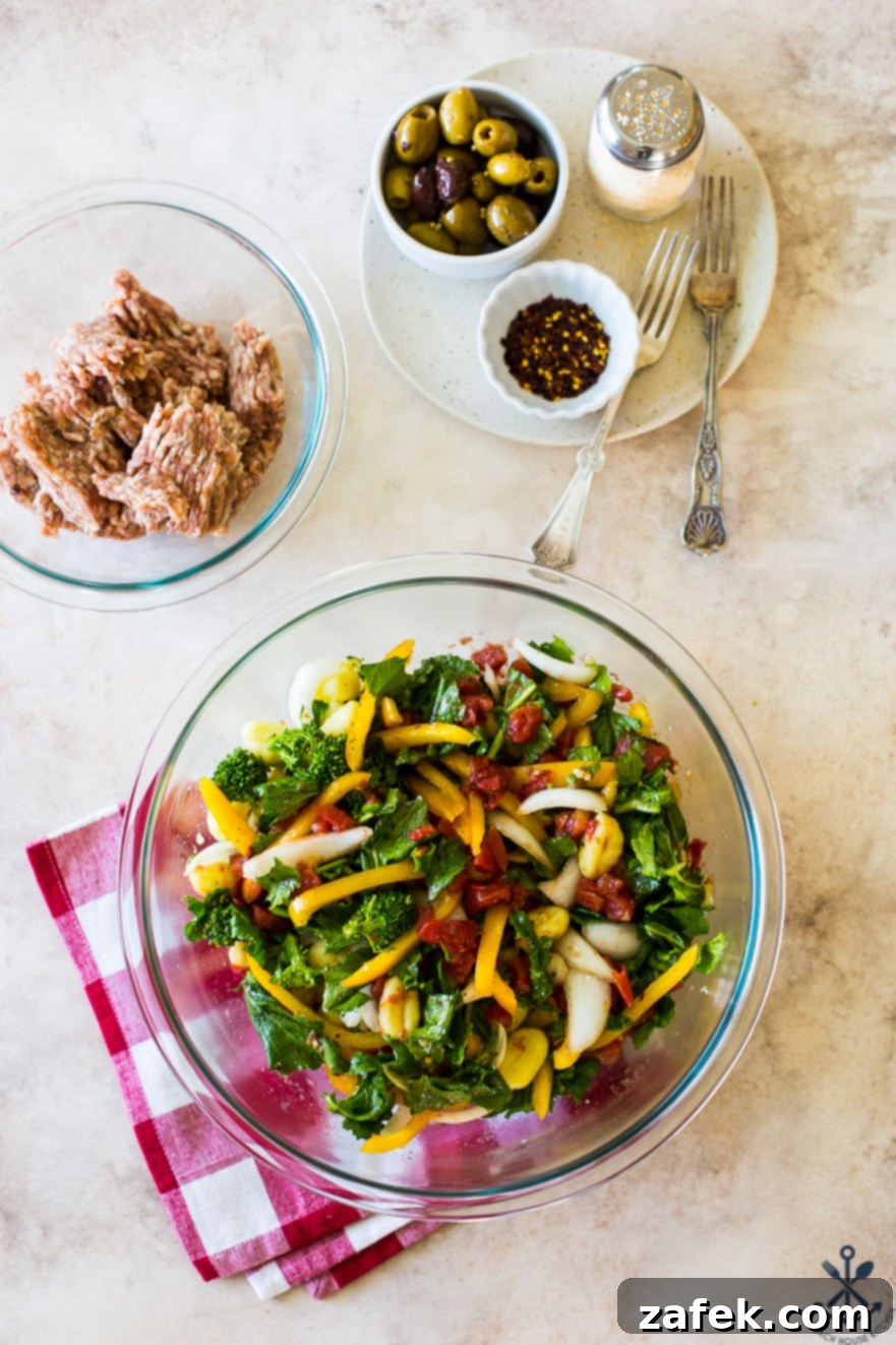Overhead photo of a bowl filled with various chopped vegetables, including broccoli rabe, bell peppers, and onions, alongside a separate bowl of raw bulk Italian sausage, illustrating the prepared ingredients.