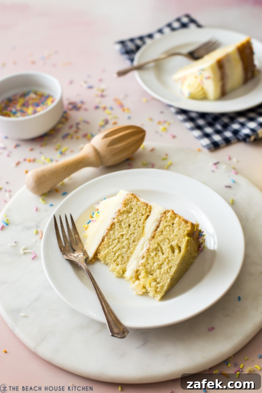 A slice of lemon cake on a plate with a fork on a round marble board, highlighting the moist texture