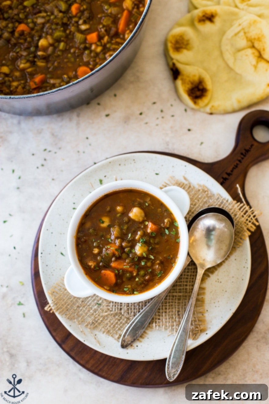 Comforting Lentil and Chickpea Soup 2 Overhead photo of a steaming bowl of lentil and chickpea soup on a rustic wooden board, garnished with fresh cilantro