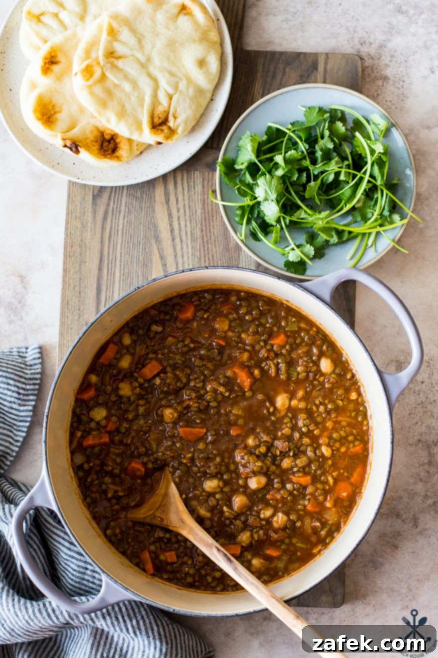 Comforting Lentil and Chickpea Soup 3 Overhead photo of a large pot of lentil and chickpea soup on a wooden board, accompanied by a plate of warm naan bread and fresh cilantro