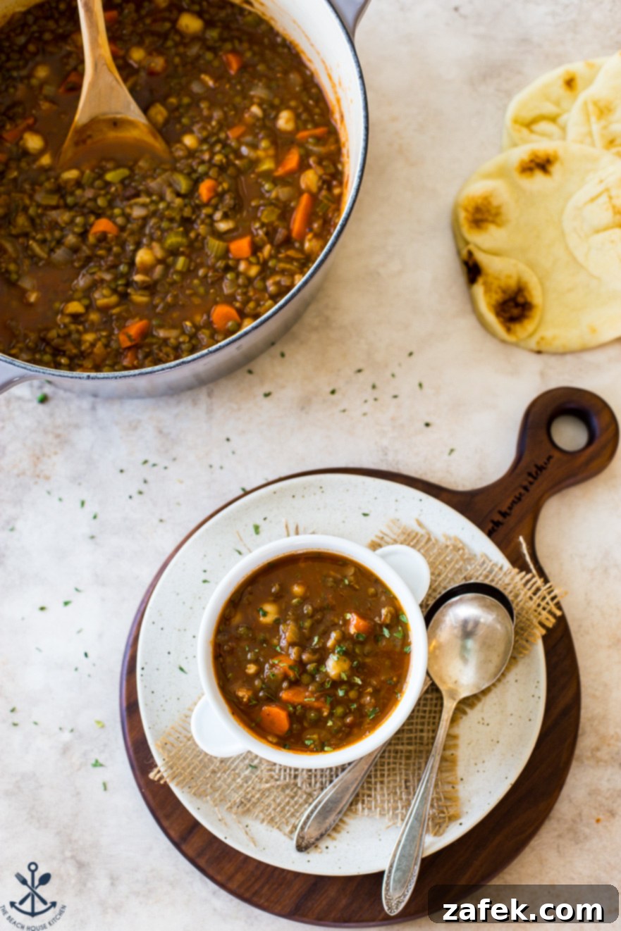 Comforting Lentil and Chickpea Soup 4 Overhead close-up of a bowl of lentil and chickpea soup on a round white serving board, with a large cooking pot blurred in the background