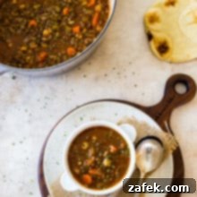 Comforting Lentil and Chickpea Soup 8 Overhead photo of a bowl of lentil soup on a round white board with a pot of soup in the background