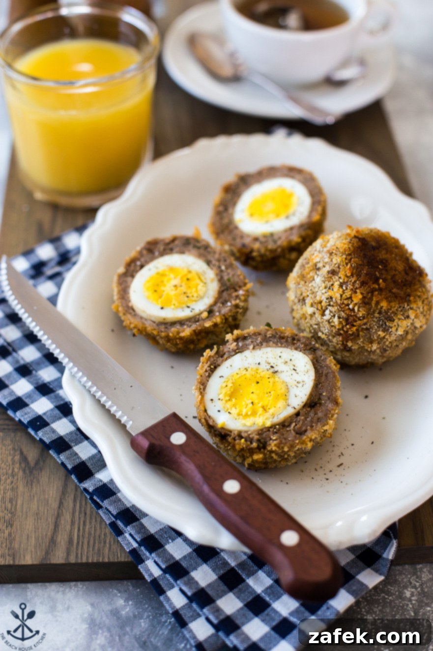 A plate with scotch eggs sliced in half with a sharp knife on a blue and white checked napkin