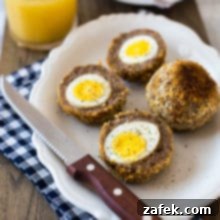 A plate with scotch eggs sliced in half with a sharp knife on a blue and white checked napkin
